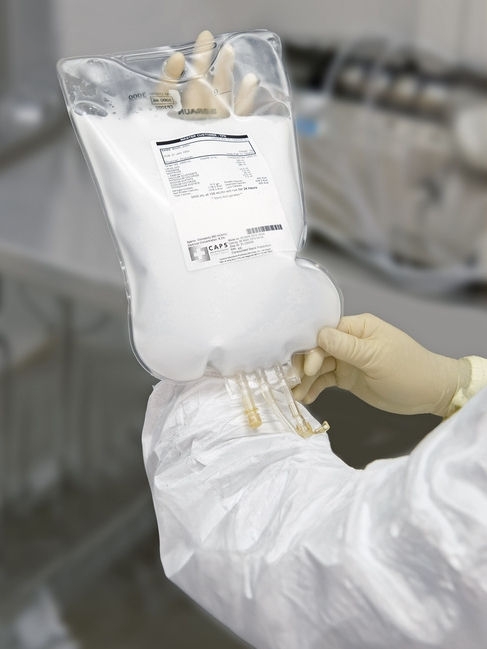 Gloved hand holding a CAPS parenteral nutrition bag in a clinical setting.