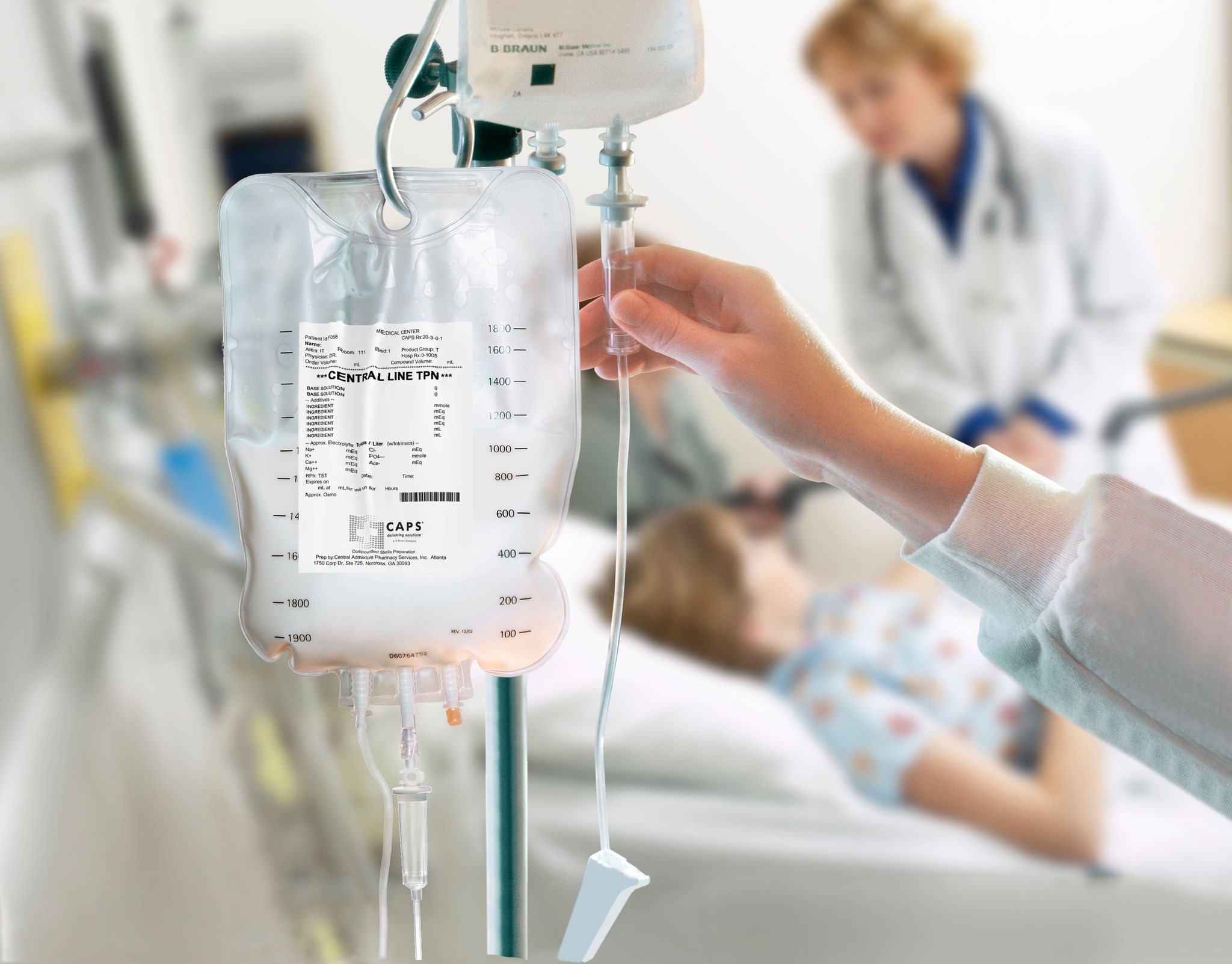 IV nutrition bag hanging on an IV pole beside a patient bed, with a healthcare professional adjusting the infusion line in a clinical setting.