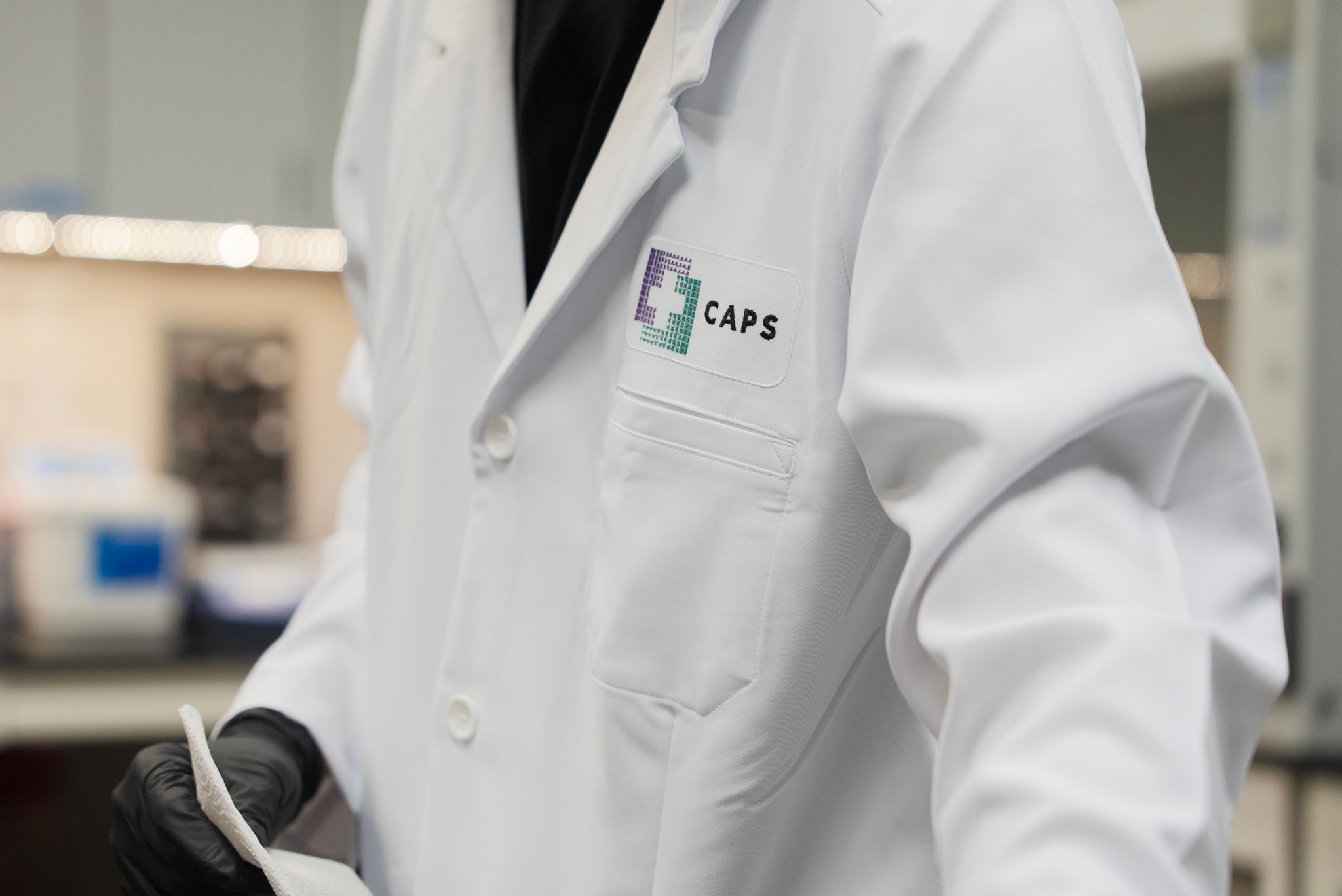 Close-up of a CAPS laboratory professional wearing a white lab coat and glove in a lab setting.