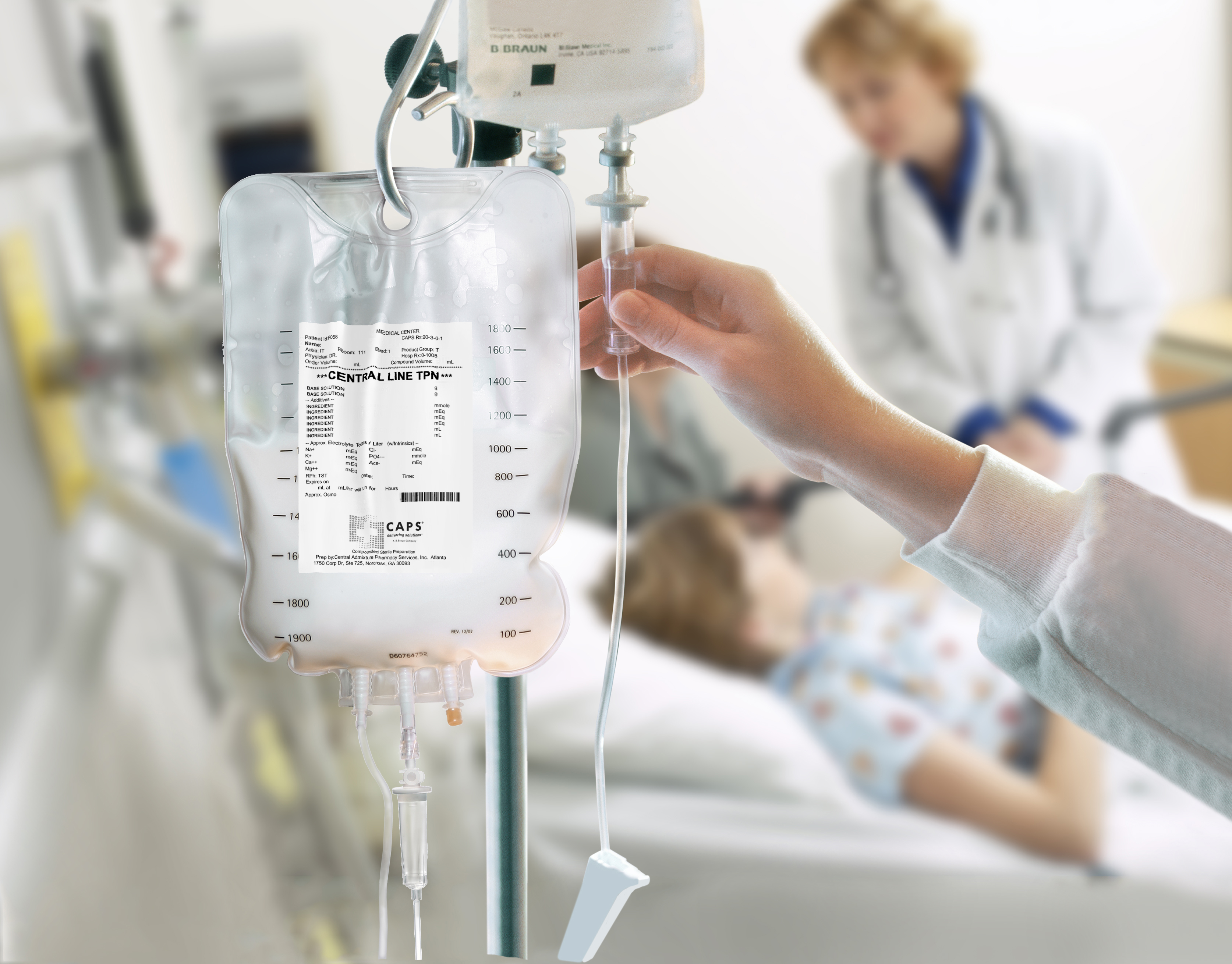IV nutrition bag hanging on an IV pole beside a patient bed, with a healthcare professional adjusting the infusion line in a clinical setting.